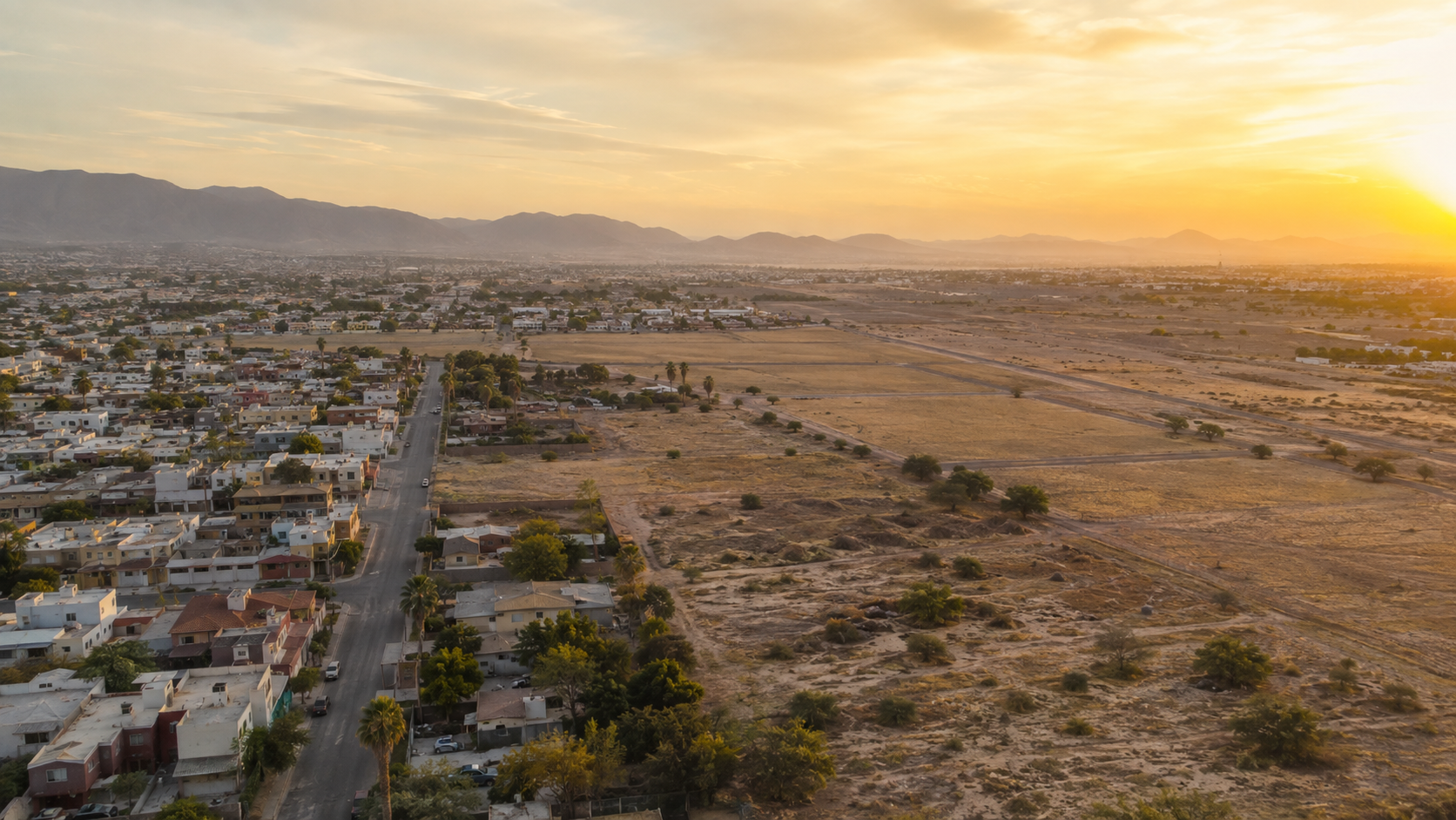 Vista aérea de una zona habitacional de Mexicali junto a terrenos en desarrollo durante la hora dorada